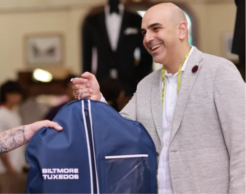 Anthony at Biltmore Tuxedos handing off a suit in blue suit protector to a client